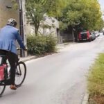 Egy bukósisakos, öltönyös férfi ekerékpárral távolodik egy városi betonúton.