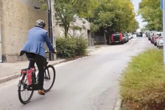 Egy bukósisakos, öltönyös férfi ekerékpárral távolodik egy városi betonúton.