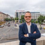 Kordos Szabolcs mosolyogva áll egy terasz korlátjánál, mögötte a Blaha Lujza tér látszik
