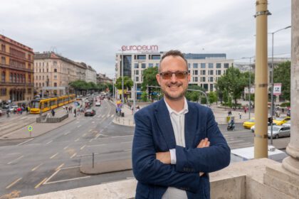 Kordos Szabolcs mosolyogva áll egy terasz korlátjánál, mögötte a Blaha Lujza tér látszik