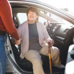 Egy 70 év feletti hölgynek segít kiszállni a sofőr egy kerületi Időstaxiból.