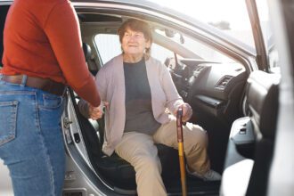 Egy 70 év feletti hölgynek segít kiszállni a sofőr egy kerületi Időstaxiból.