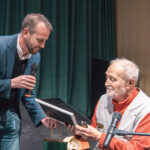 Dr. Juhász Árpád éppen egy keretezett képet vesz a kezébe, melyet vendéglátója ad át neki a beszélgetés során.