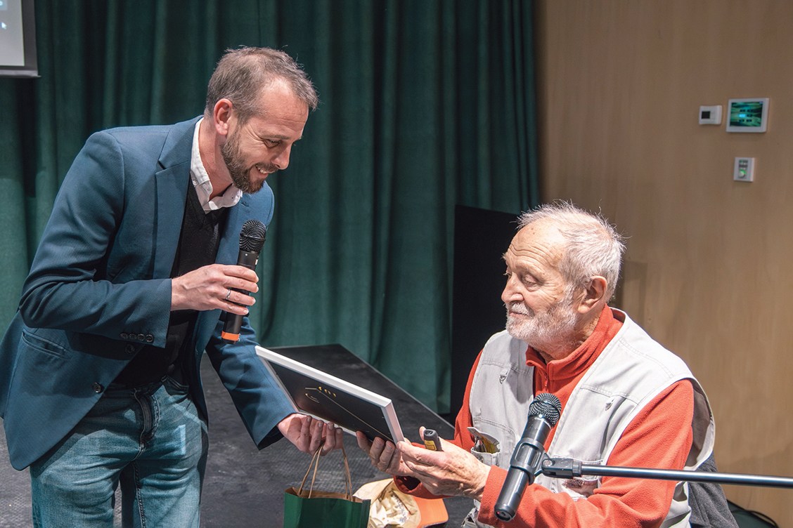 Dr. Juhász Árpád éppen egy keretezett képet vesz a kezébe, melyet vendéglátója ad át neki a beszélgetés során.